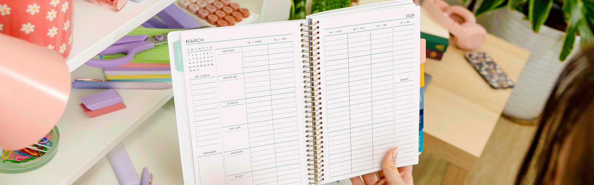 Student planner being held open to a weekly spread with a desk with accessories behind it