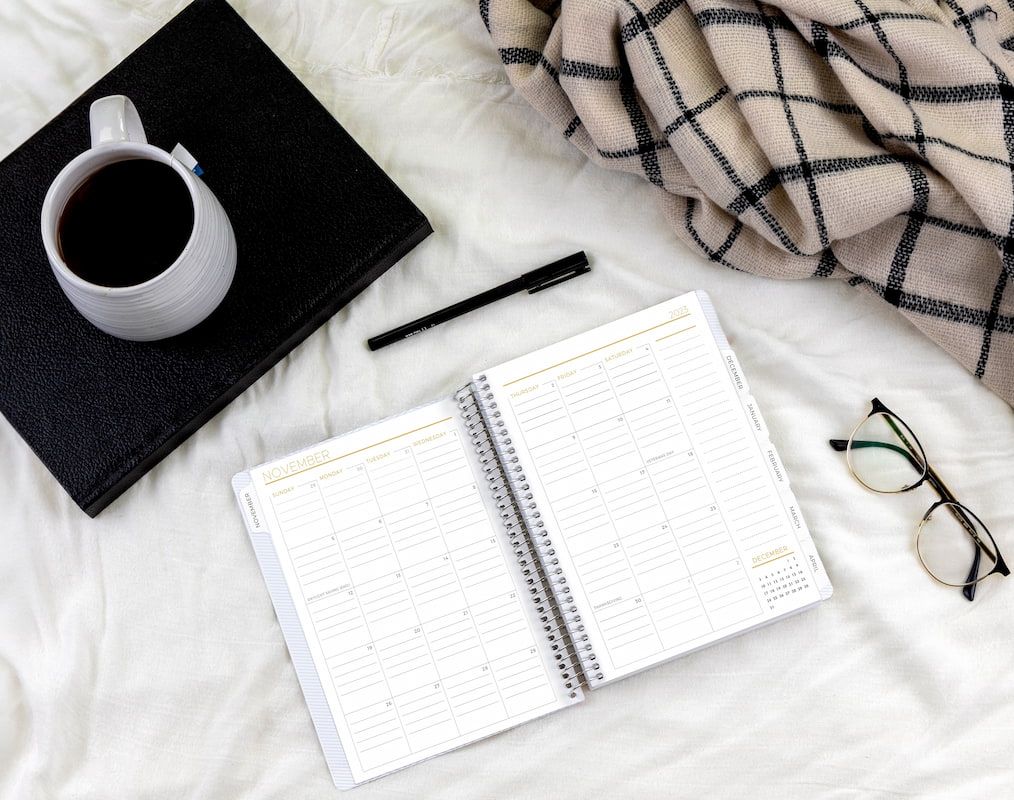 Modern planner open, cup of coffee, pen, glasses and cozy blanket
