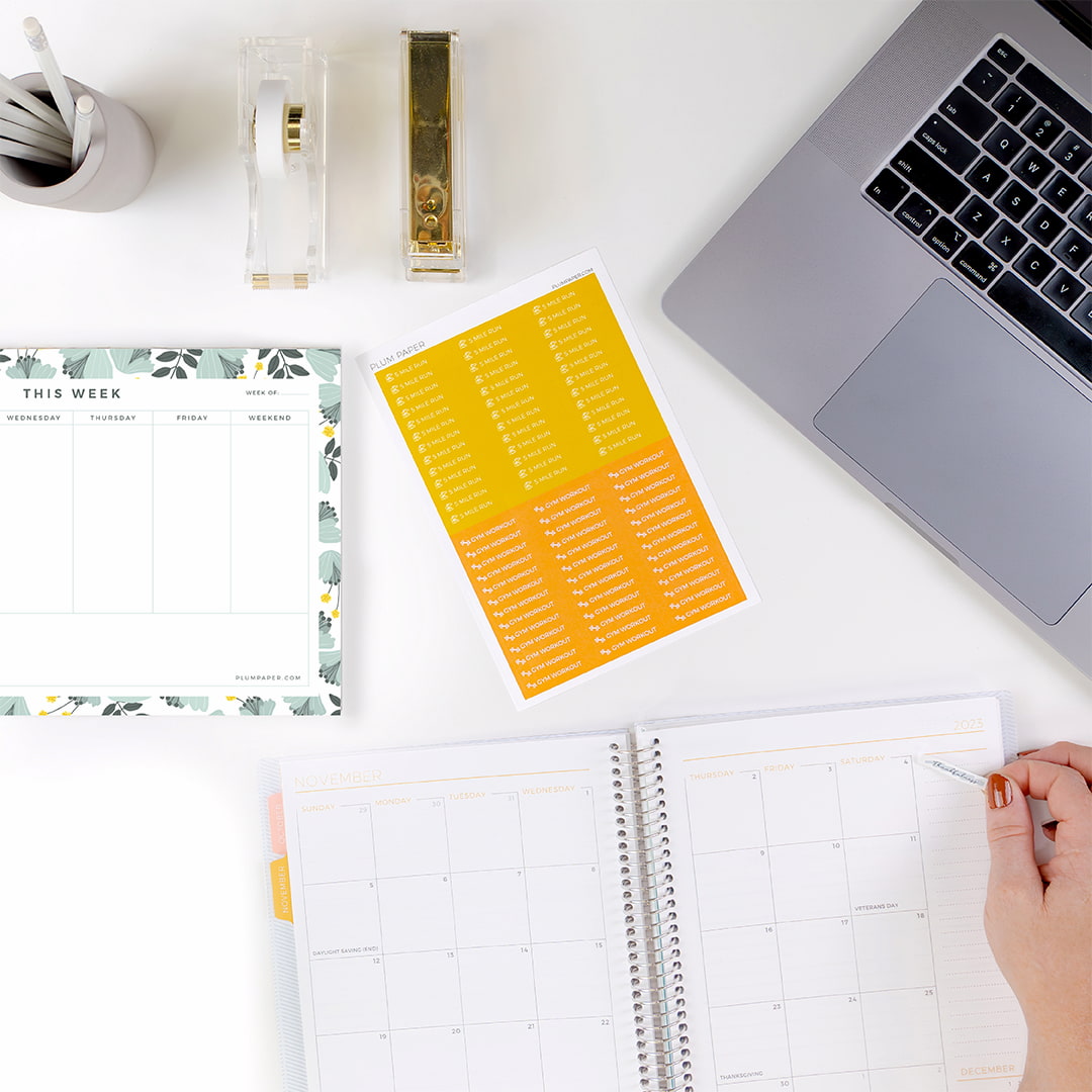 Desktop scene, modern planner with sticking being placed, notepad, planner stickers  laptop, office supplies