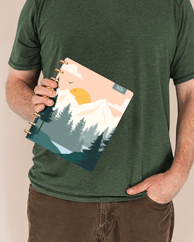 Person holding a planner with a mountain and sun design Person holding a planner with a mountain and sun design
