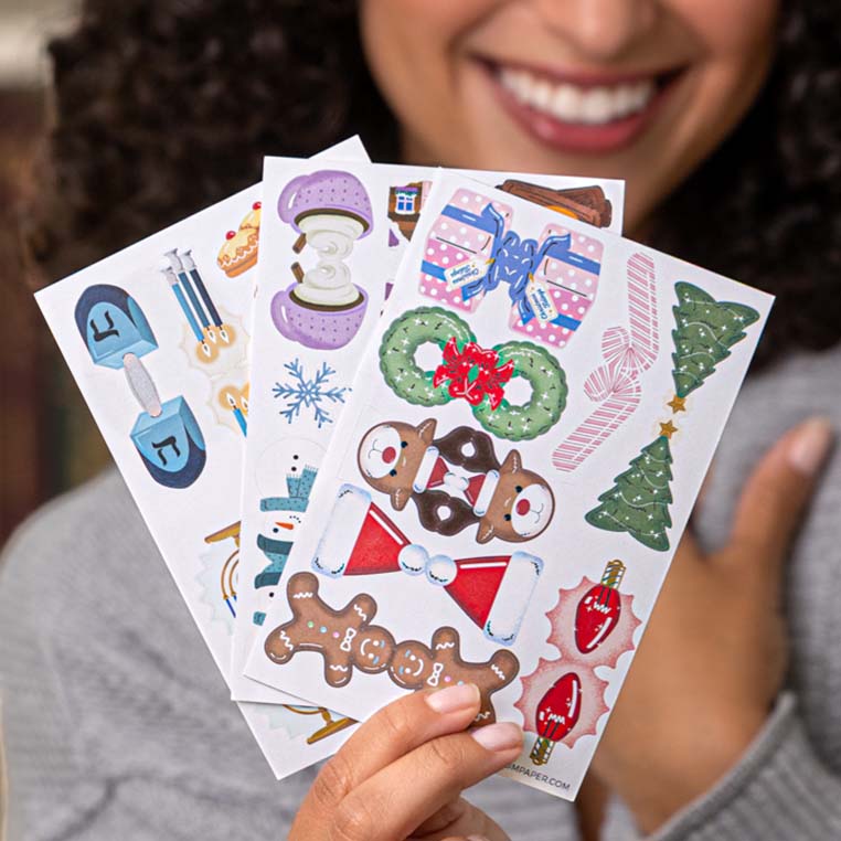 Smiling woman holding Plum Paper holiday sticker sheets featuring gingerbread men, snowflakes, Christmas trees, and festive icons — creative accessories for handmade planners and 2026 custom planner gift sets. Smiling woman holding Plum Paper holiday sticker sheets featuring gingerbread men, snowflakes, Christmas trees, and festive icons — creative accessories for handmade planners and 2026 custom planner gift sets.