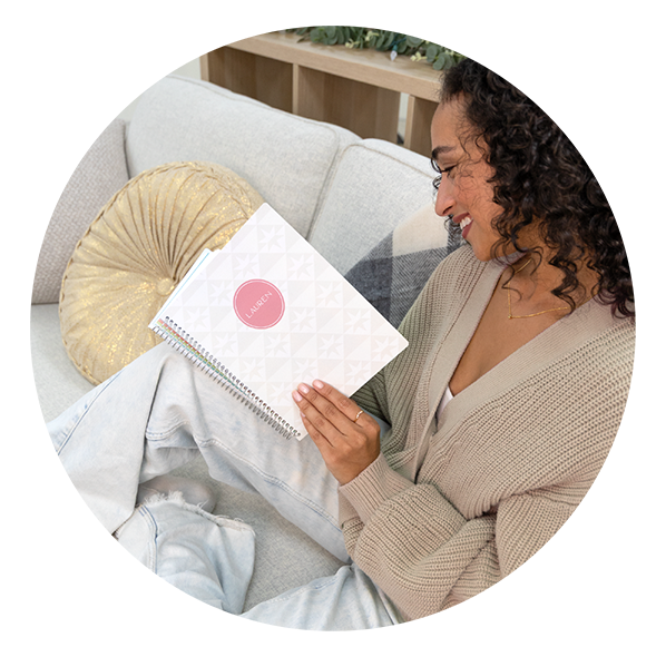 Woman relaxing on a sofa holding a minimalist white geometric Plum Paper custom planner labeled in pink — a 2026 handmade planner designed for journaling, goal-setting, and calm, intentional living. Woman relaxing on a sofa holding a minimalist white geometric Plum Paper custom planner labeled in pink — a 2026 handmade planner designed for journaling, goal-setting, and calm, intentional living.