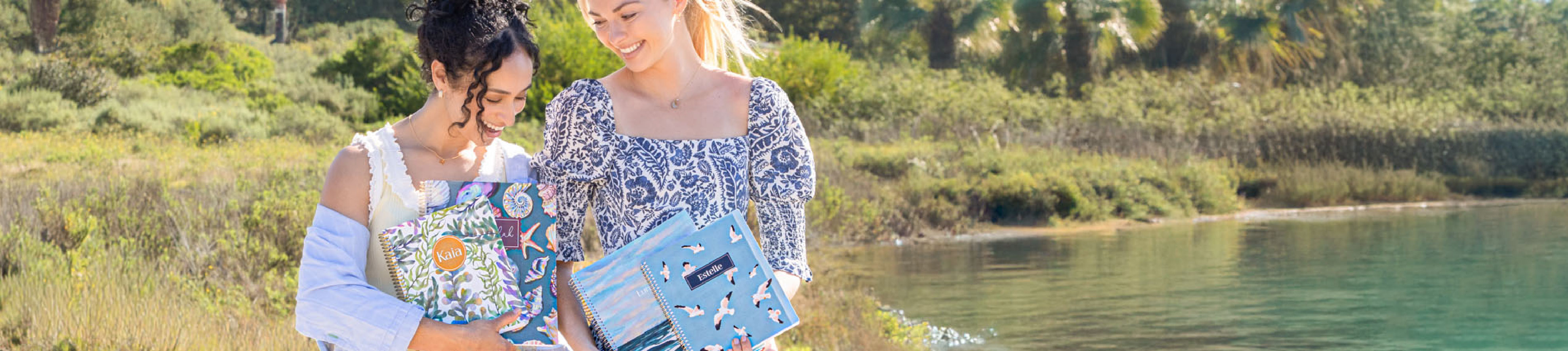 Two women outdoors holding planners and notebooks in a bright, summer setting