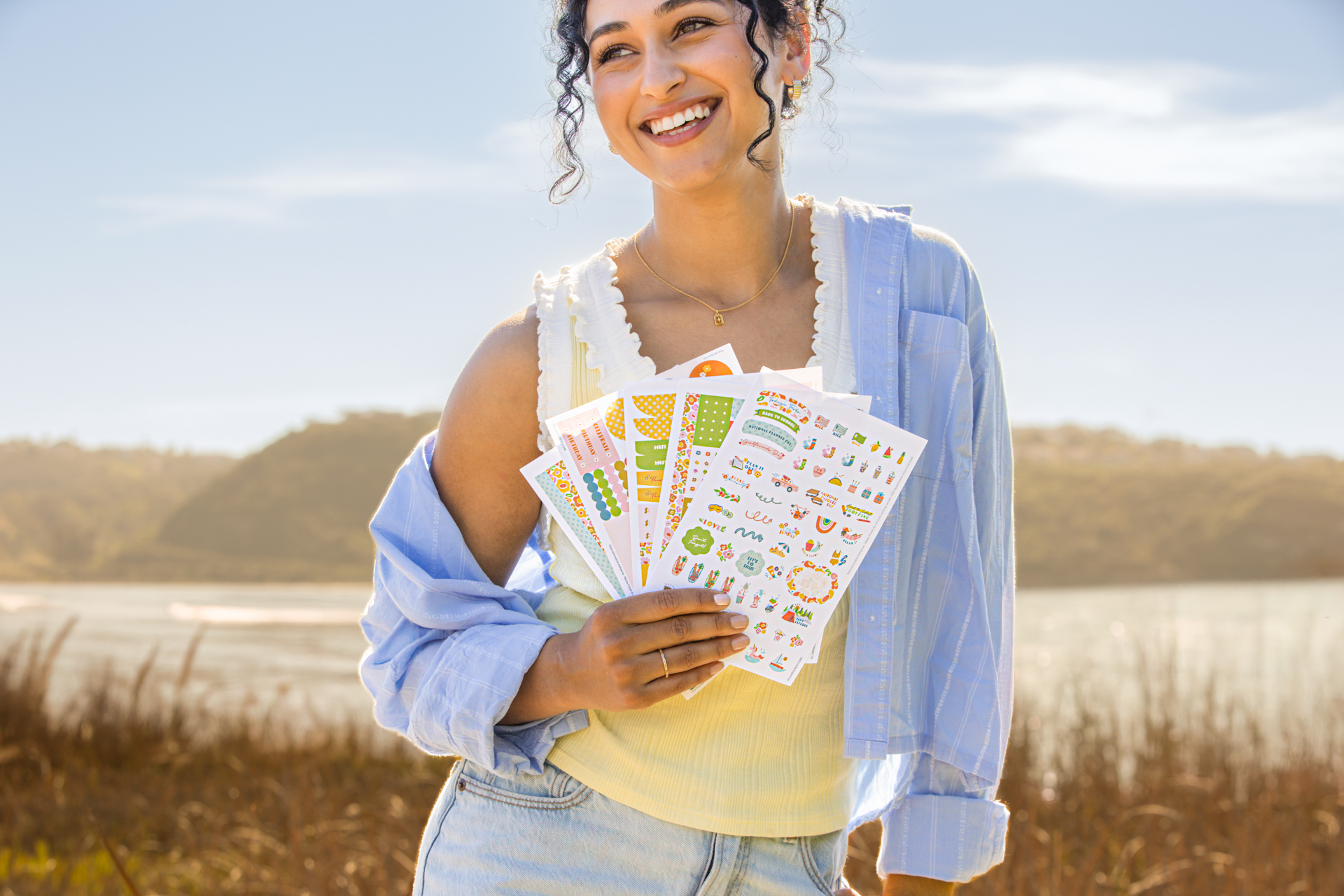 Woman outdoors holding pages from a colorful sticker kit for planners