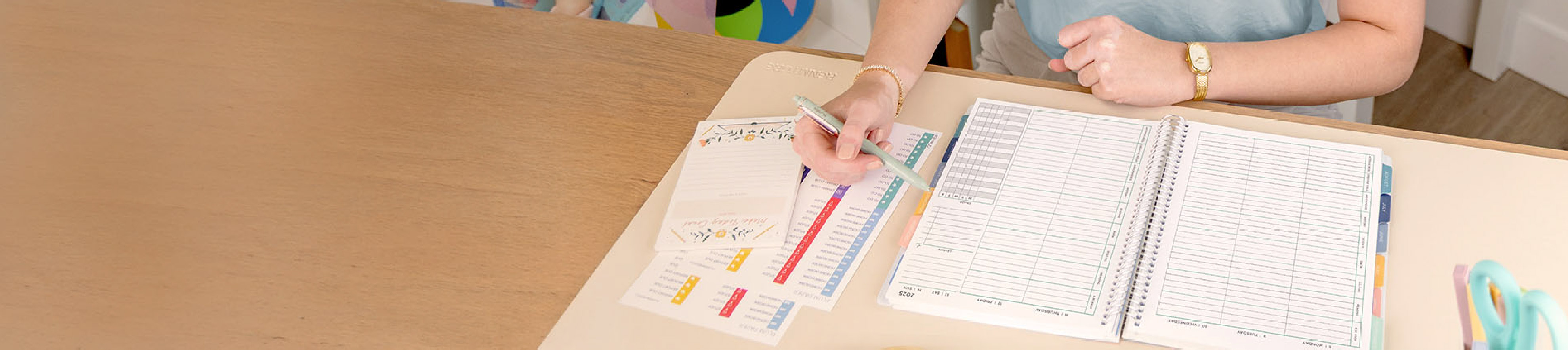 Woman sitting at a desk holding a pencil with an open, coiled planner, stickers, and notepad Woman sitting at a desk holding a pencil with an open, coiled planner, stickers, and notepad
